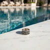 Silver ring with ornate design, by pool.