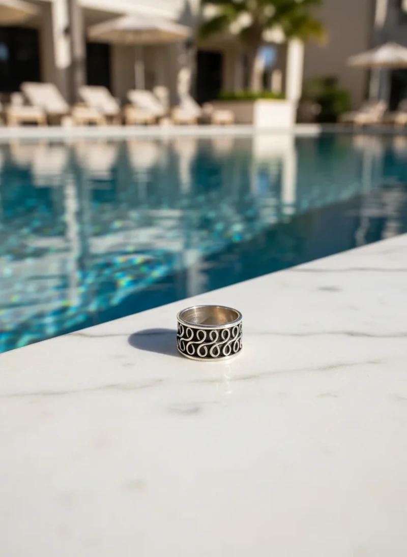 Silver ring with ornate design, by pool.