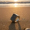 Silver patterned signet ring on sandy beach.