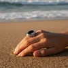 Silver ring with black onyx stone on beach sand.
