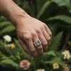 Silver square ring with stitched detail on a hand.
