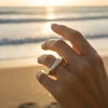 Hand model wearing modern geometric silver ring at sunset beach.