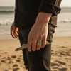 Man's hand on beach wearing silver crown ring.
