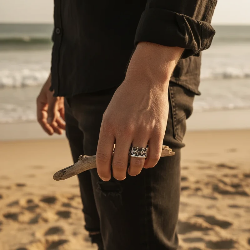 Man's hand on beach wearing silver crown ring.