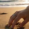 Hand wearing ornate silver ring on beach.