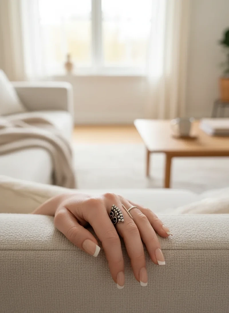 Woman's hand with silver ring on beige sofa.
