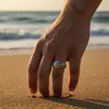 Hand wearing ornate ring touching beach sand.