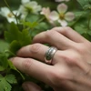 Silver ring with ornate design, worn on hand.