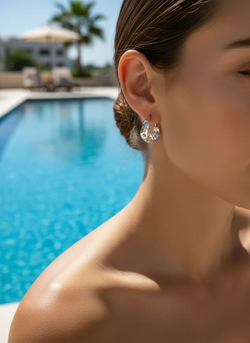 Woman's ear wearing silver cutout hoop earrings.