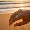 Hand model wearing gold ring with blue gemstone on beach at sunset.