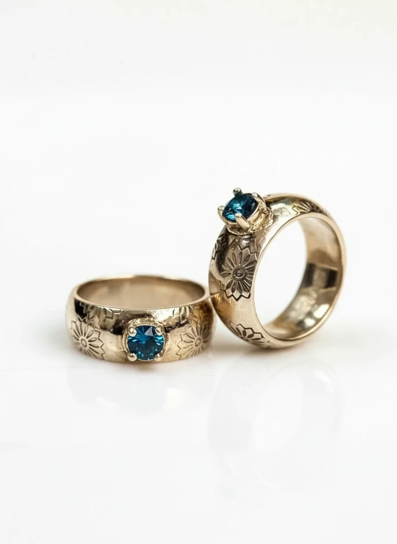Pair of gold rings with blue gemstones and floral engraving.